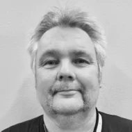 Svart-hvitt hodeskudd av en mann med grånende hår, bart og fippskjegg, iført mørk t-skjorte.