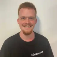 Bjørn-Erik-Moe-rotated-e1599550093349-300x300 En mann med kort, rødt hår og skjegg smiler til kameraet, iført en svart T-skjorte med hvit tekst med teksten "Lässenteet" mot en ensfarget, lys bakgrunn.
