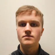 En ung mann med kort, lysebrunt hår ser rett inn i kameraet mot en ensfarget, lys bakgrunn.