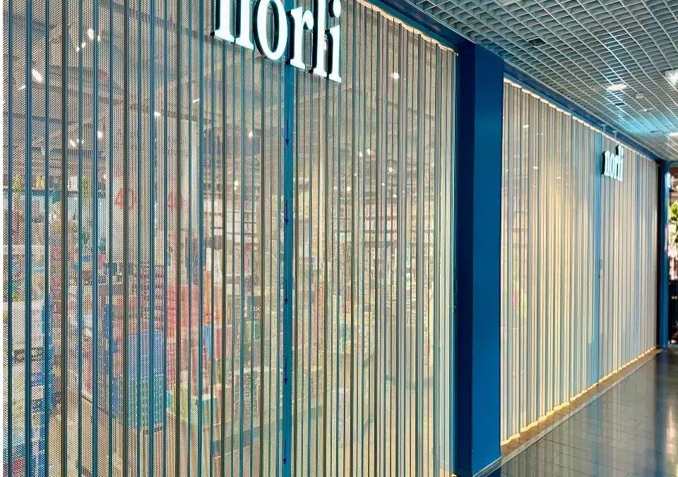 En butikk med et delvis synlig skilt med påskriften "nori" er avstengt av en metallgittersjalusi inne på et kjøpesenter. Hyller og produkter er synlige gjennom gitteret.