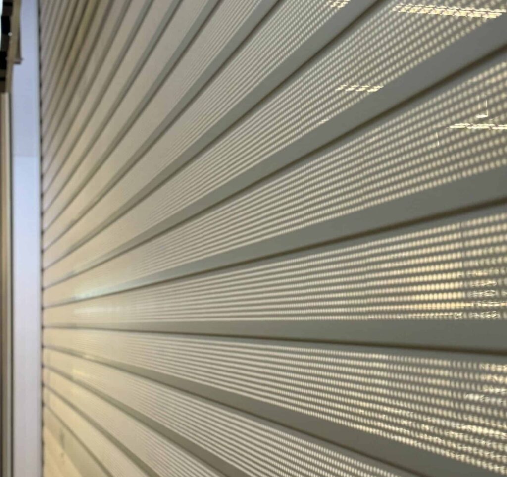 Nærbilde av horisontale metallplater med perforerte linjer, som minner om en gitterdesign, og som fremhever intrikate lys- og skyggemønstre.