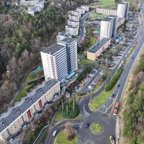 Flyfoto av boligblokker, parkeringsplasser og en svingete vei omgitt av trær og grøntområder.