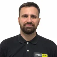 Marko-Tomasevic En mann med kort, brunt hår og skjegg, iført svart skjorte med "tryggerom"-logo, står mot en hvit bakgrunn.
