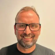 Morten-Bergene-1-300x300 En mann med kort hår, skjegg og briller smiler til kameraet mot en ensfarget, lys bakgrunn.