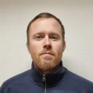 Ole-Gunnar-300x300 En mann med kort, lysebrunt hår, trimmet skjegg og et nøytralt ansiktsuttrykk bærer en mørk jakke med glidelås mot en ensfarget, lys bakgrunn.