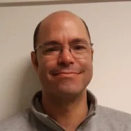 Øyvind En mann med briller og vikende hårfeste, iført en lysegrå genser med glidelås, står foran en enkel, offwhite bakgrunn og smiler lett til kameraet.