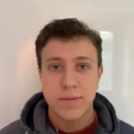 Pawel-300x300 En ung person med kort, brunt hår og mørk hettegenser står vendt mot kameraet mot en enkel, hvit bakgrunn.