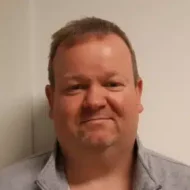 Tor-Oddvar-300x300 En mann med kort, lysebrunt hår og lyst skjegg står foran en hvit vegg, iført en grå skjorte med krage.