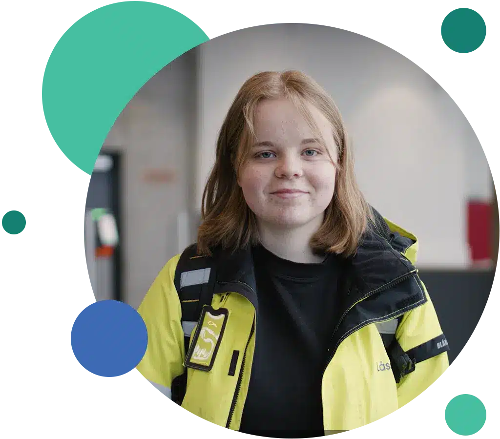 En person med skulderlangt, lysebrunt hår i gul og svart jakke står innendørs, vendt mot kameraet og smiler lett. Geometriske former rammer inn bildet.