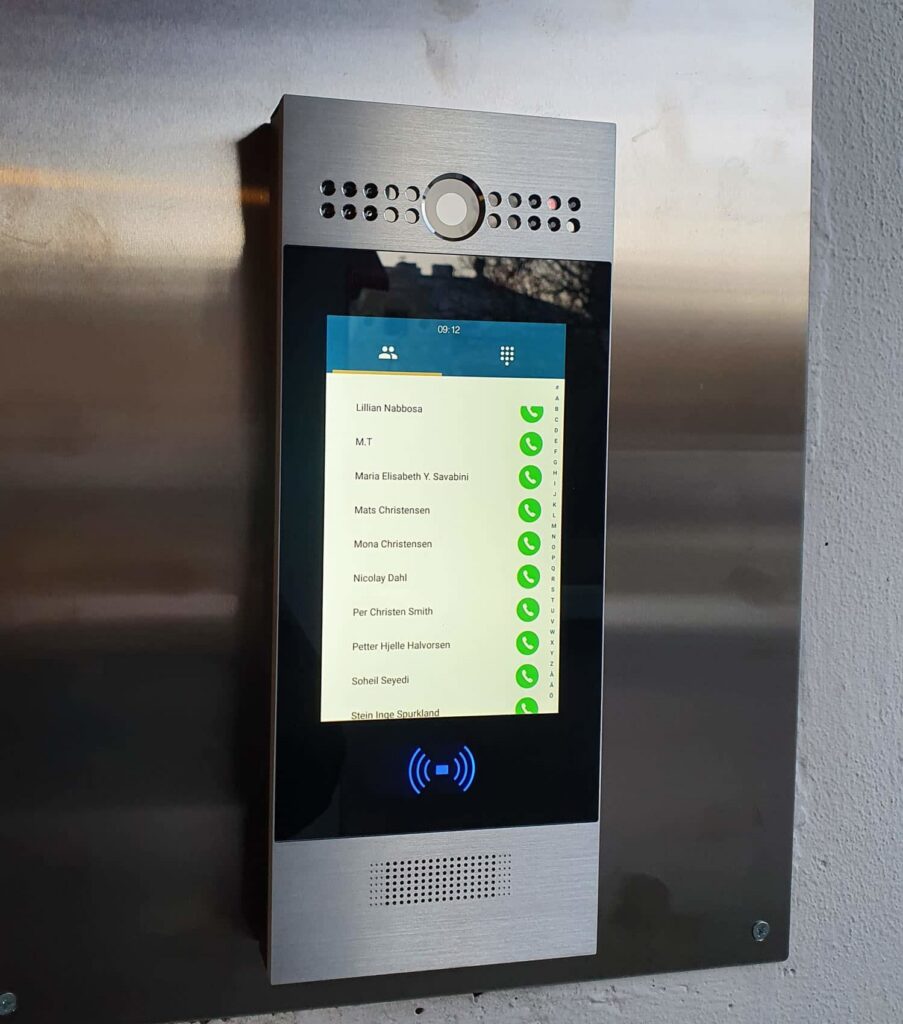 steplock-1500x1700 Et digitalt intercom-system montert på en vegg viser en liste med navn med grønne haker ved siden av hvert navn på berøringsskjermen.